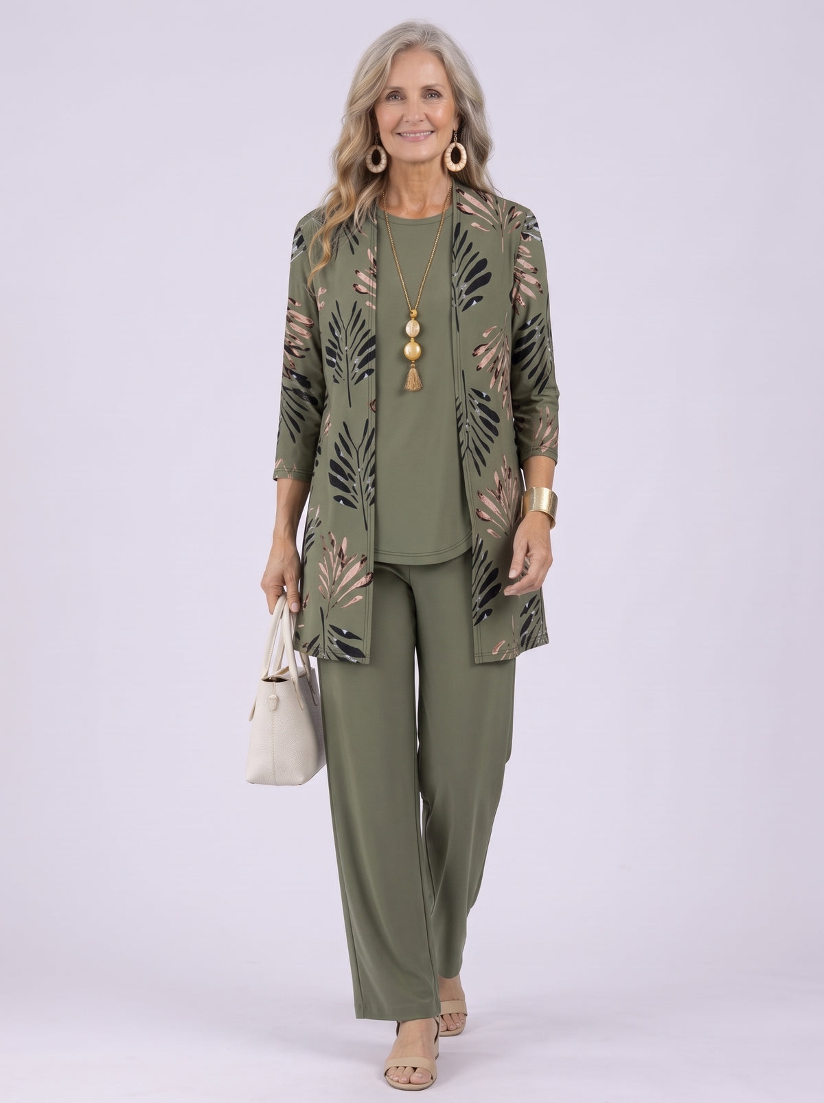Donna con completo verde oliva: cardigan lungo con stampa di foglie nere e rosa, top girocollo e pantalone ampio, mentre cammina